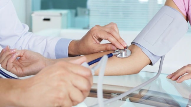 Profissional da saúde aferindo pressão arterial de paciente mulher.