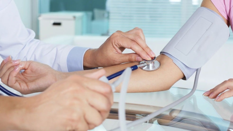 Profissional da saúde aferindo pressão arterial de paciente mulher.