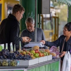 Banca de frutas no terminal de ônibus de Jundiaí com permissionários atendendo clientes e variedade de frutas frescas expostas.