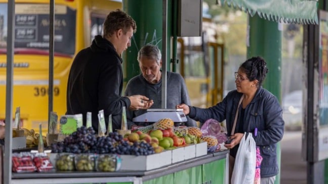 Banca de frutas no terminal de ônibus de Jundiaí com permissionários atendendo clientes e variedade de frutas frescas expostas.