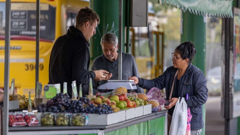 Banca de frutas no terminal de ônibus de Jundiaí com permissionários atendendo clientes e variedade de frutas frescas expostas.