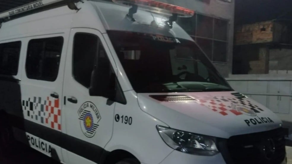 Viatura da Polícia Militar de São Paulo estacionada à noite, com luz de emergência acesa e identificação de Base Comunitária Móvel.