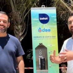 Dois homens sorriem ao lado de um ponto de hidratação recém-instalado na Avenida 9 de Julho, em Jundiaí, com palmeiras ao fundo.