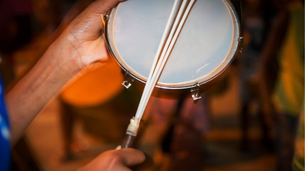 Pessoa tocando tamborim com baqueta múltipla em ambiente iluminado, destacando detalhes do instrumento e do movimento. Pessoa tocando tamborim com baqueta múltipla em ambiente iluminado, destacando detalhes do instrumento e do movimento.