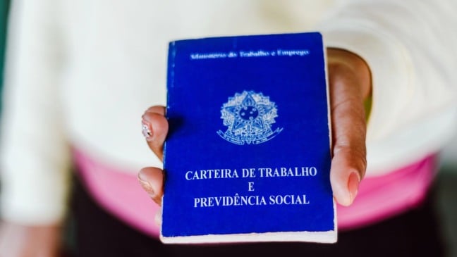 Pessoa segurando uma Carteira de Trabalho e Previdência Social azul em destaque.