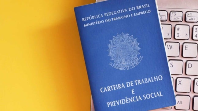 Carteira de Trabalho e Previdência Social sobre teclado de notebook com fundo amarelo, simbolizando oportunidades de emprego.