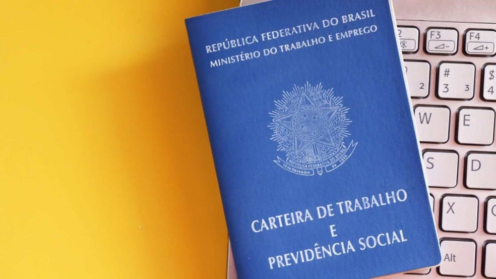 Carteira de Trabalho e Previdência Social sobre teclado de notebook com fundo amarelo, simbolizando oportunidades de emprego.