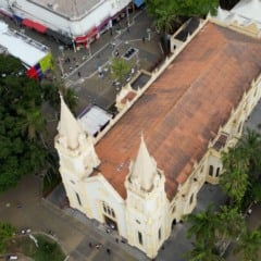 Vista aérea da Igreja Matriz Nossa Senhora do Desterro e da praça central de Jundiaí, cercada por árvores, comércios e ruas movimentadas.