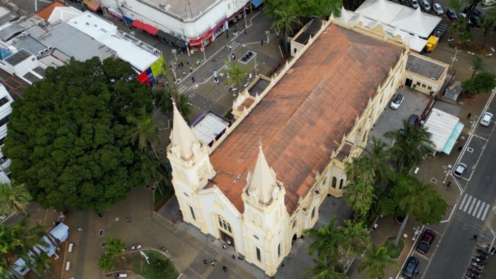 Vista aérea da Igreja Matriz Nossa Senhora do Desterro e da praça central de Jundiaí, cercada por árvores, comércios e ruas movimentadas.