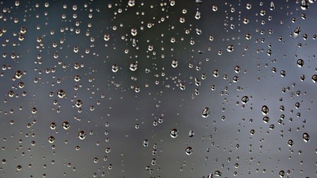 Gotas de chuva em um vidro com fundo cinza desfocado, simbolizando tempo nublado e possibilidade de chuva.