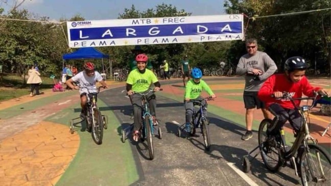 Crianças com bicicletas adaptadas largam em prova do Festival Regional de Ciclismo do PEAMA no Parque da Cidade, em Jundiaí, sob a faixa de “Largada”.