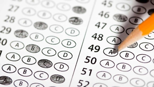 Pessoa preenchendo cartão de respostas de prova de múltipla escolha com lápis, representando um processo seletivo ou concurso.