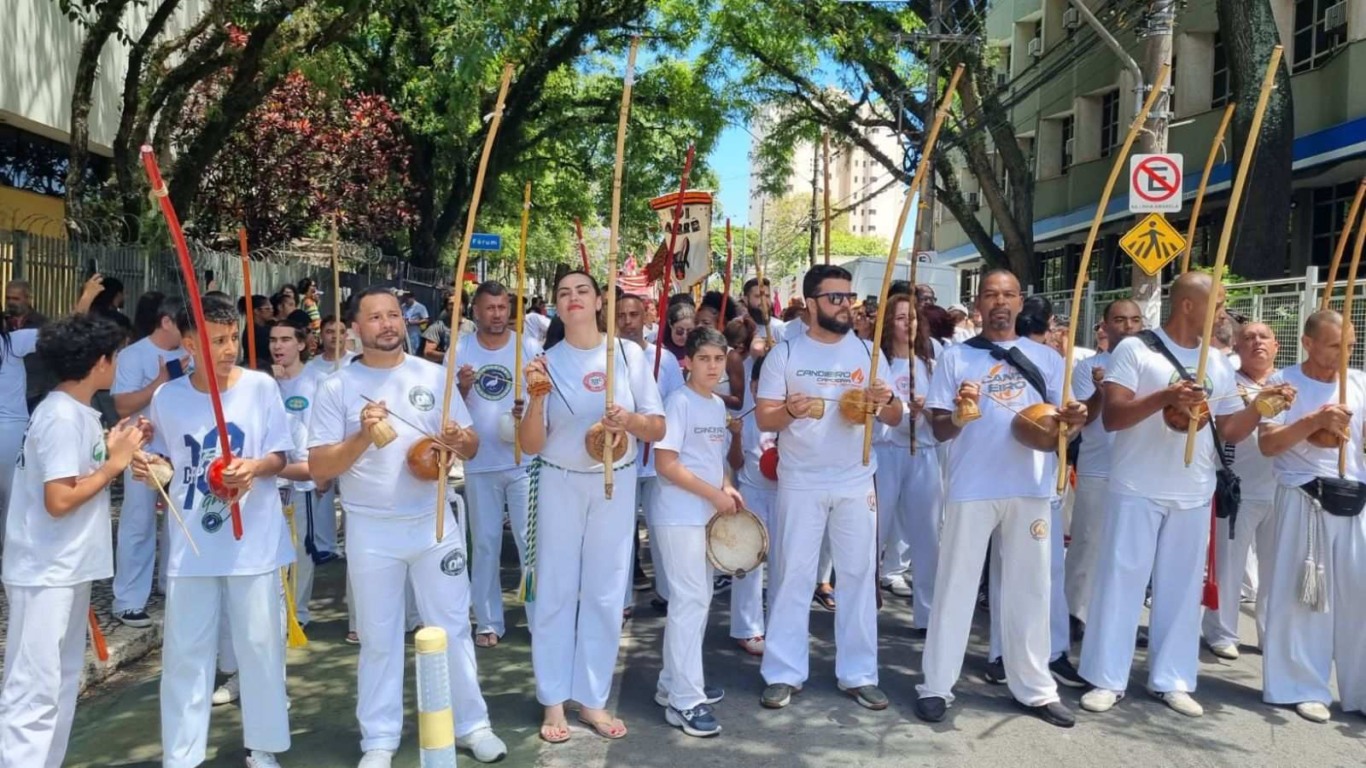 Grupo de capoeiristas vestidos de branco tocando berimbaus e acompanhando a Marcha da Consciência Negra pelas ruas de Jundiaí.