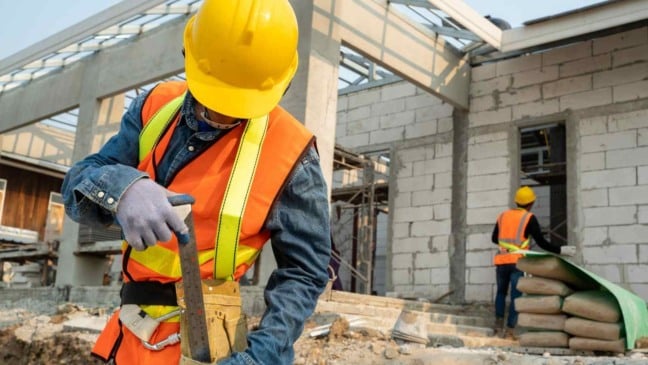 Operários da construção civil usando capacete e colete refletivo enquanto trabalham em um canteiro de obras em Jundiaí.