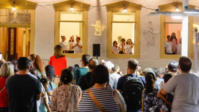 Coral se apresenta nas janelas iluminadas do Solar do Barão em Jundiaí durante evento de Natal, com público reunido na calçada assistindo.