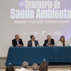 Mesa de autoridades durante o VIII Seminário de Saúde Ambiental dos Comitês PCJ em Jundiaí, com painel projetado ao fundo e público assistindo.