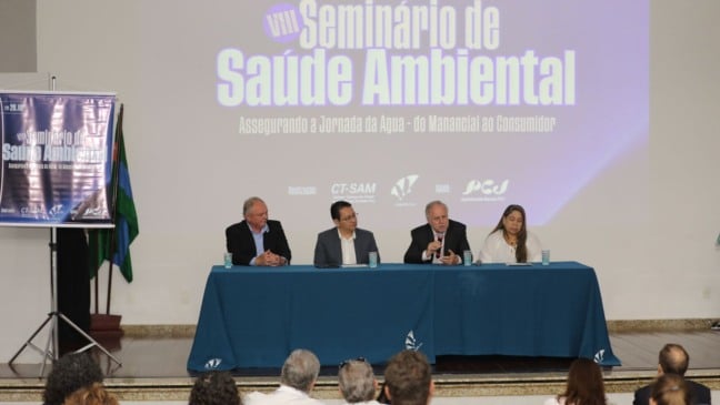 Mesa de autoridades durante o VIII Seminário de Saúde Ambiental dos Comitês PCJ em Jundiaí, com painel projetado ao fundo e público assistindo.