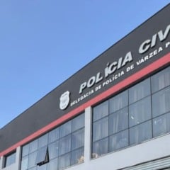 Fachada da Delegacia de Polícia Civil de Várzea Paulista vista de baixo, com o letreiro e o céu azul ao fundo.