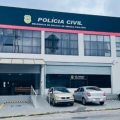 Fachada da Delegacia de Polícia de Várzea Paulista, com carros estacionados em frente e o letreiro da Polícia Civil visível no topo do prédio.
