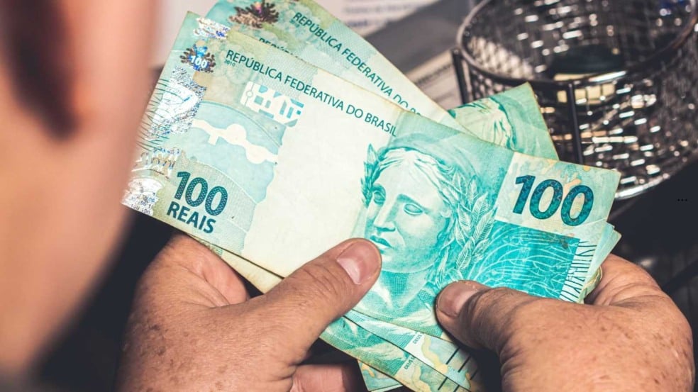 Mãos segurando cédulas de 100 reais, representando pagamento ou movimentação de dinheiro no Brasil. Mãos segurando cédulas de 100 reais, representando pagamento ou movimentação de dinheiro no Brasil.