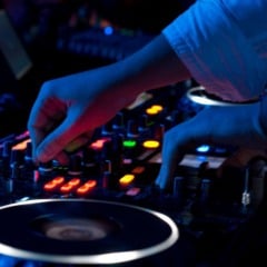 DJ ajustando mesa de som iluminada em ambiente escuro com luzes coloridas.