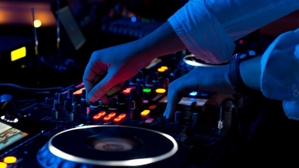 DJ ajustando mesa de som iluminada em ambiente escuro com luzes coloridas. DJ ajustando mesa de som iluminada em ambiente escuro com luzes coloridas.