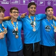 Quatro atletas do Time Jundiaí de Natação exibem medalhas conquistadas no Paulista Infantil diante do painel oficial da competição.
