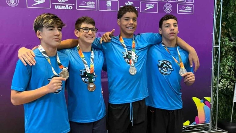 Quatro atletas do Time Jundiaí de Natação exibem medalhas conquistadas no Paulista Infantil diante do painel oficial da competição. Quatro atletas do Time Jundiaí de Natação exibem medalhas conquistadas no Paulista Infantil diante do painel oficial da competição.