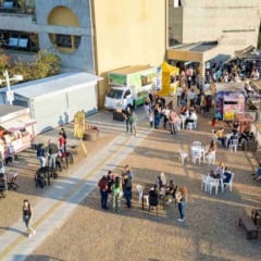Vista aérea do evento Sexta no Paço em Jundiaí, com food trucks, tendas gastronômicas, mesas ocupadas pelo público e a fachada do Paço Municipal ao fundo.
