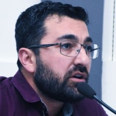 Vereador Faouaz Taha fala ao microfone durante sessão na Câmara de Jundiaí, usando óculos e camisa roxa.