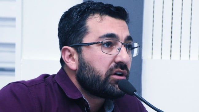 Vereador Faouaz Taha fala ao microfone durante sessão na Câmara de Jundiaí, usando óculos e camisa roxa.