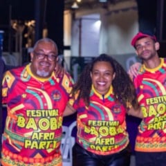 Grupo de cinco pessoas vestindo camisetas coloridas do Festival Baobá Afro Party, sorrindo e celebrando a cultura afro-brasileira.