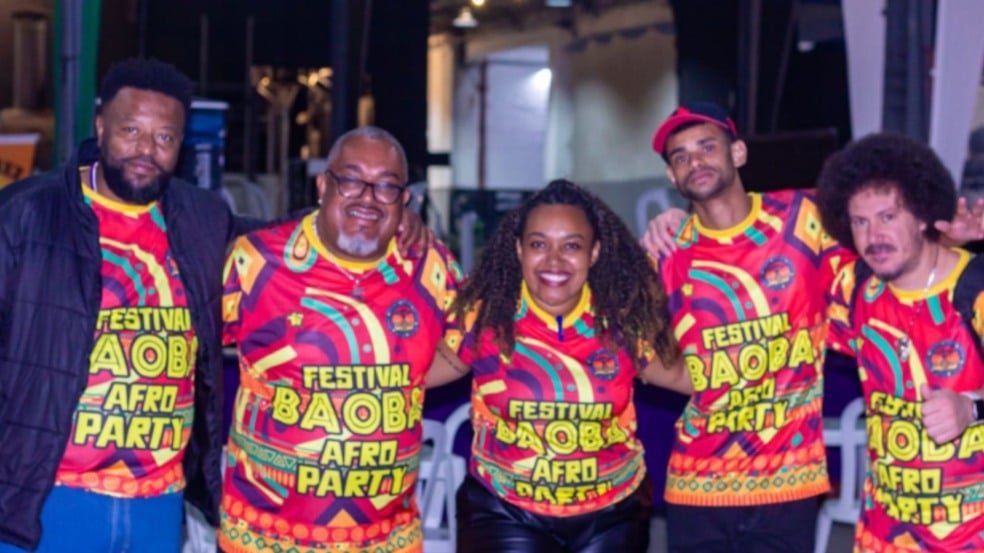 Grupo de cinco pessoas vestindo camisetas coloridas do Festival Baobá Afro Party, sorrindo e celebrando a cultura afro-brasileira.