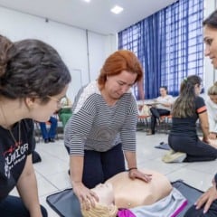 Gestora escolar realiza manobra de RCP em boneco durante treinamento de primeiros socorros em Jundiaí, com orientação de estudantes da FMJúnior.