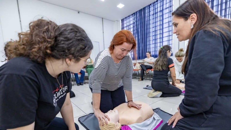 Gestora escolar realiza manobra de RCP em boneco durante treinamento de primeiros socorros em Jundiaí, com orientação de estudantes da FMJúnior.