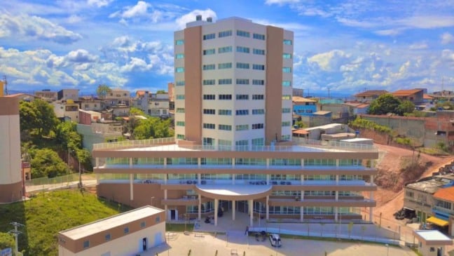 Prédio da Prefeitura de Francisco Morato visto de frente, com fachada moderna, janelas amplas e bairro residencial ao redor sob céu azul com nuvens.