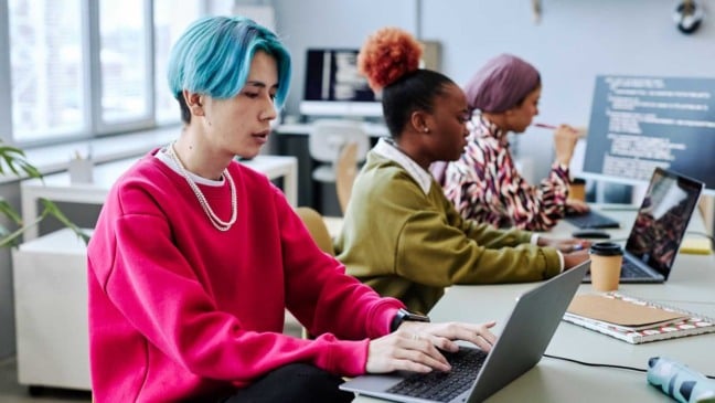 Jovens da Geração Z trabalhando em laptops em um escritório moderno, simbolizando diversidade e inovação tecnológica.