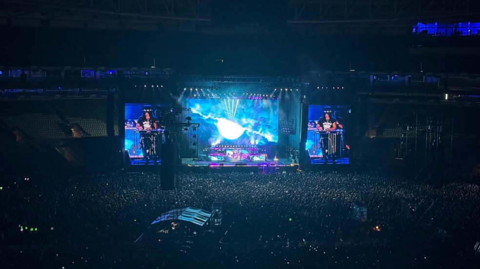 Show do Guns N’ Roses com Axl Rose cantando no telão e Slash tocando guitarra, diante de um estádio lotado iluminado em vermelho.