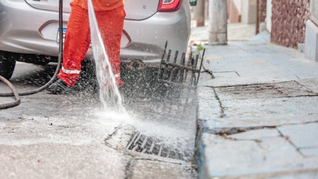 Funcionário da Prefeitura realiza limpeza de boca de lobo com jato de água para desobstruir a drenagem urbana em Jundiaí.