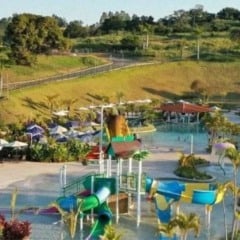 Vista de um parque aquático com piscinas, escorregadores infantis, guarda-sóis e áreas verdes ao redor, em ambiente de resort.