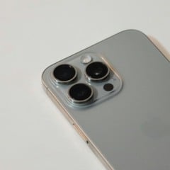 Close da traseira de um iPhone prata, evidenciando o módulo com três lentes de câmera.