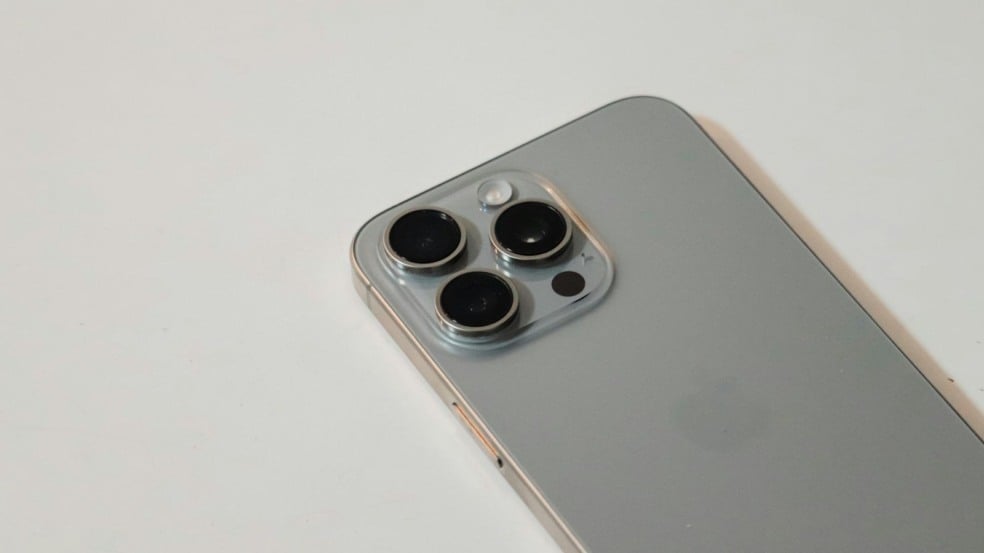 Close da traseira de um iPhone prata, evidenciando o módulo com três lentes de câmera.