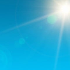 Céu azul sem nuvens com o sol forte no canto superior direito e raios de luz se espalhando.