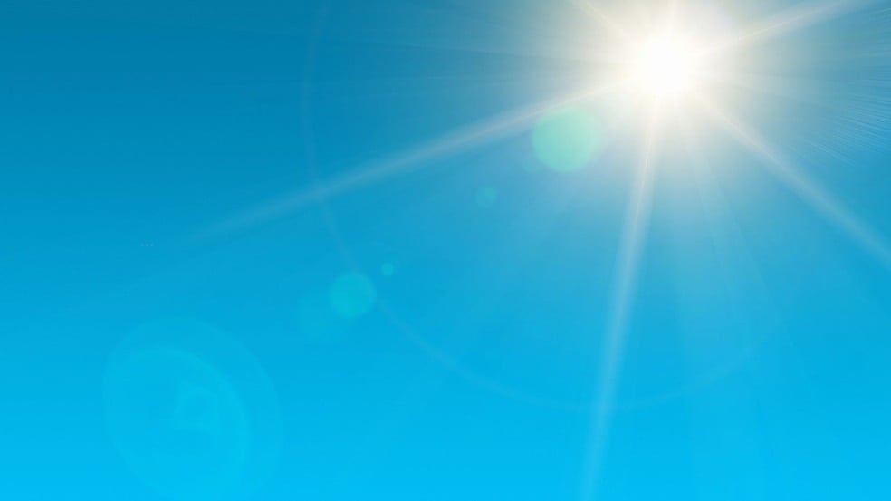 Céu azul sem nuvens com o sol forte no canto superior direito e raios de luz se espalhando.