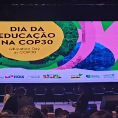 Telão do “Dia da Educação na COP30” em um auditório, com pessoas circulando à frente do palco antes do início das atividades.