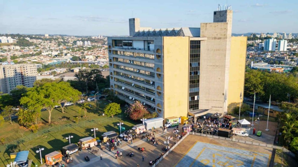 Vista aérea do Paço Municipal de Jundiaí, com a praça em frente ocupada por food trucks e visitantes, e a cidade ao fundo ao entardecer.