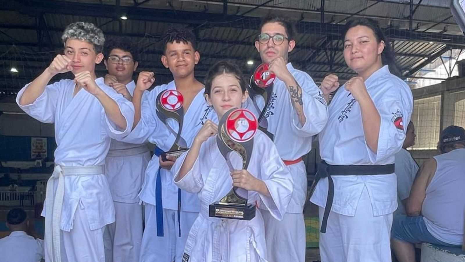 Seis atletas do projeto social de Jundiaí seguram troféus e fazem pose de karatê após conquistas no Campeonato Brasileiro.