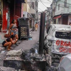 Mulheres observam carro incendiado em favela do Rio após megaoperação policial