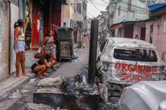 Mulheres observam carro incendiado em favela do Rio após megaoperação policial