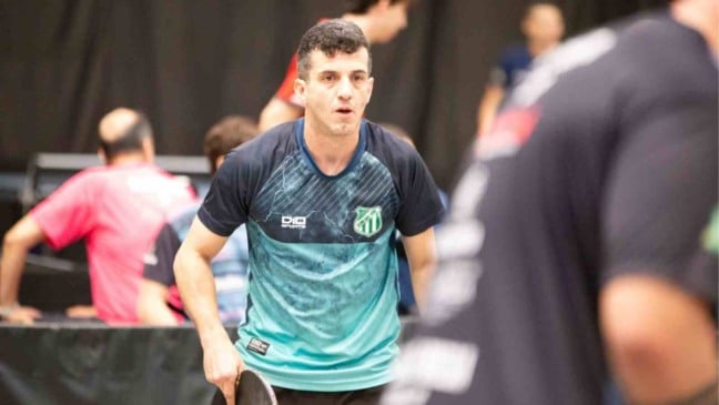 Michel Sartorato, do Time Jundiaí, joga tênis de mesa durante competição estadual, vestindo uniforme azul e verde.